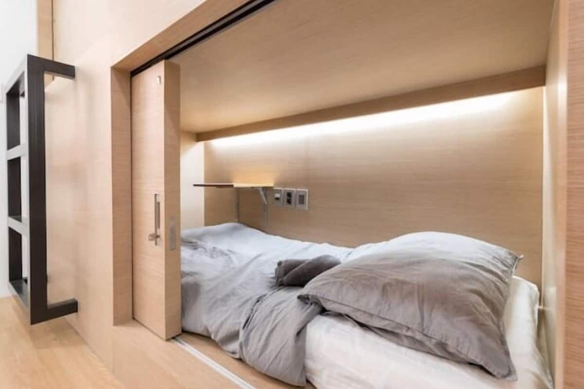 A compact room with a bed, a small bedside table, and a wall-mounted light fixture.