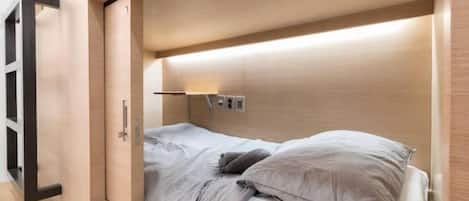 A compact room with a bed, a small bedside table, and a wall-mounted light fixture.