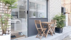 A modern building with a glass door, a small outdoor seating area with wooden chairs, and potted plants. - The Stay Simple (Seoul)