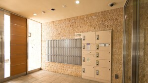 A hotel lobby with a marble wall, a metal elevator, and numbered lockers. - At RLiS House Namba Minami (Osaka)