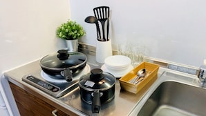 A compact kitchen with a stove, pots, a sink, and a small potted plant. - At RLiS House Namba Minami (Osaka)