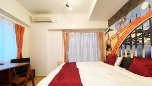 A hotel room with a bed, a desk, and a chair. There is a window with curtains, an air conditioning unit, and a wall with a mural. - At RLiS House Namba Minami (Osaka)