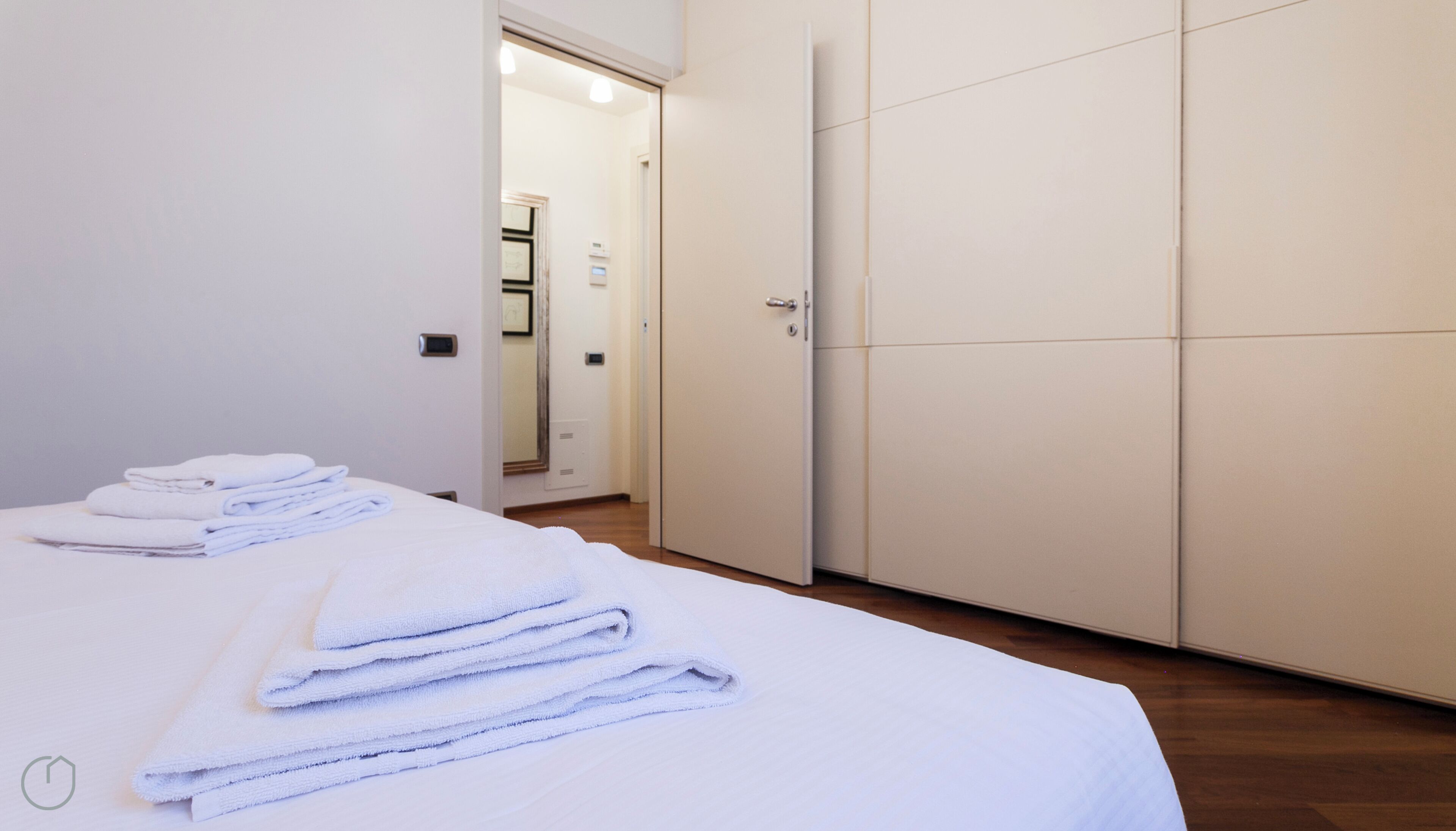 A hotel room with a bed, a wardrobe, and a bathroom visible through an open door.