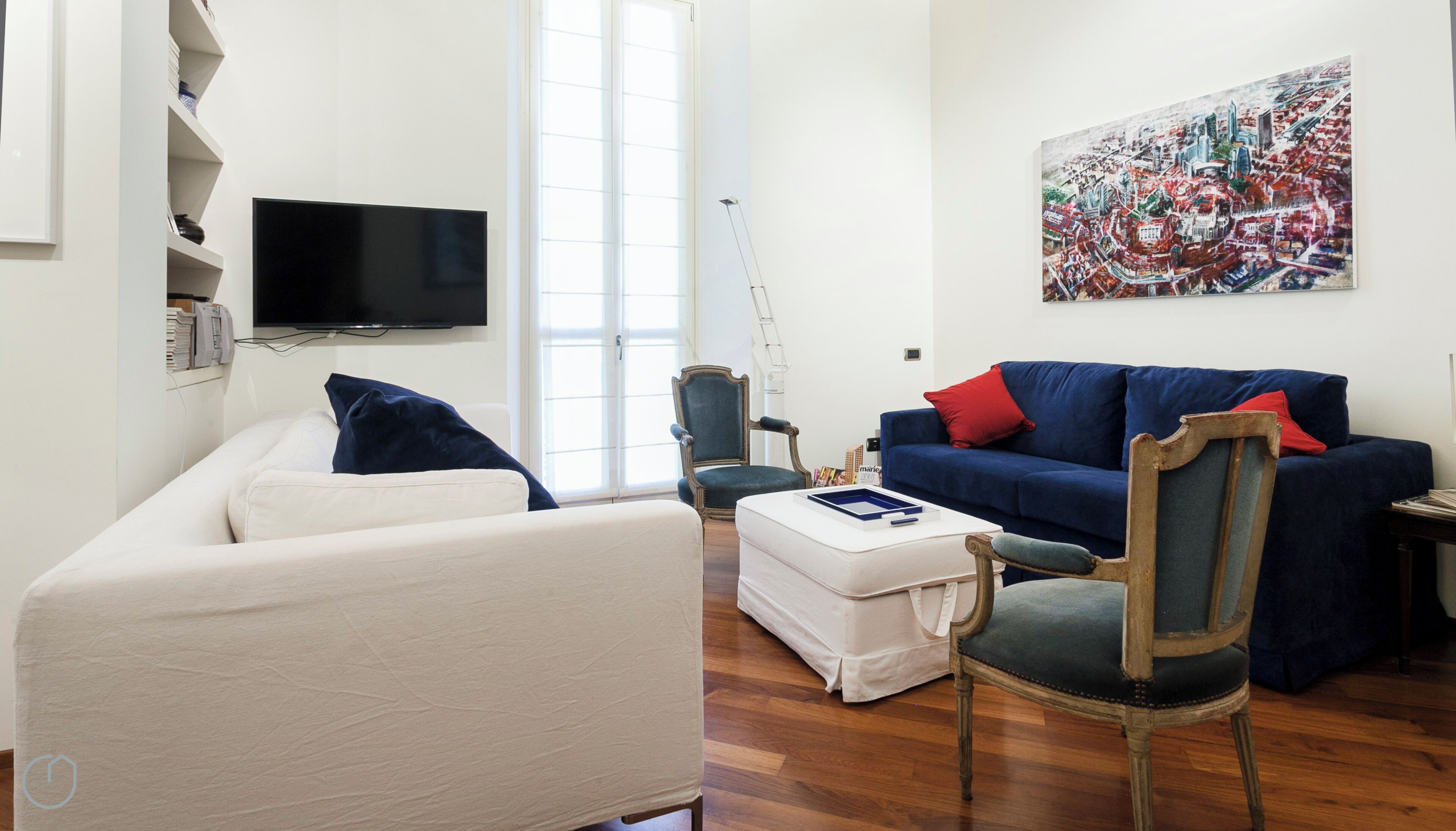 Un salon comprenant un canapé, un fauteuil, un pouf et un tableau accroché au mur.