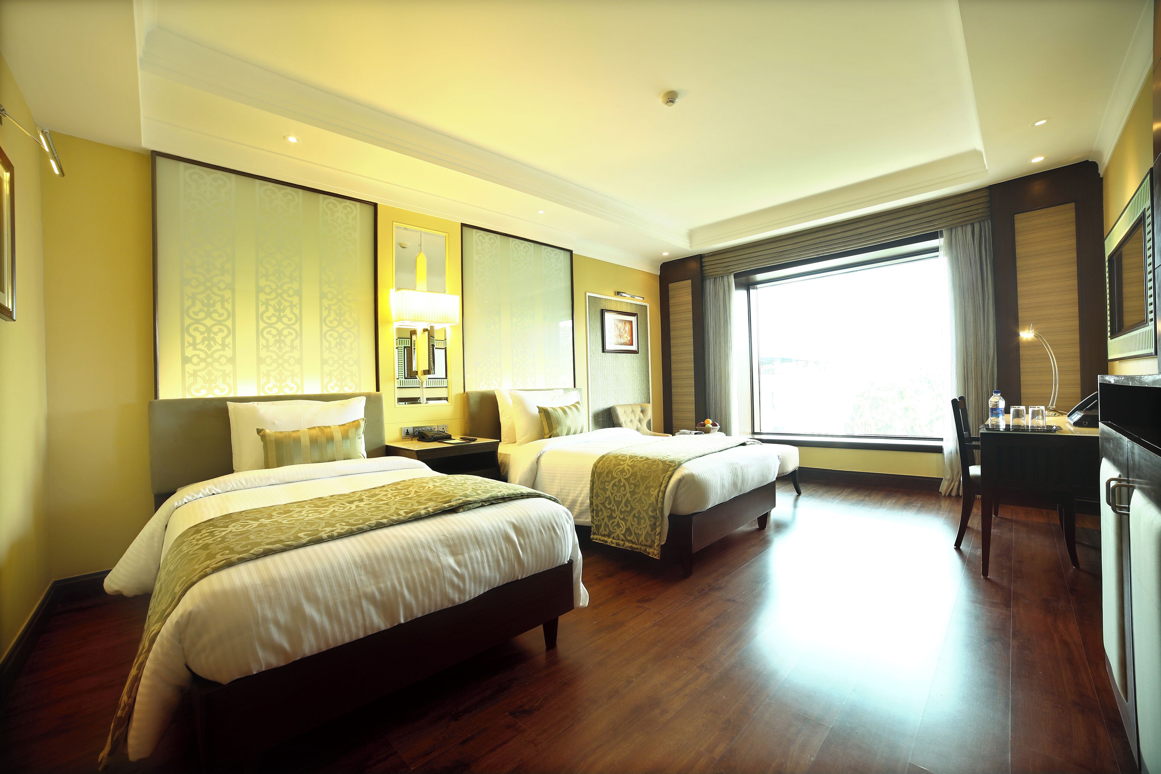Habitación de hotel con dos camas, un escritorio y un ventanal amplio.