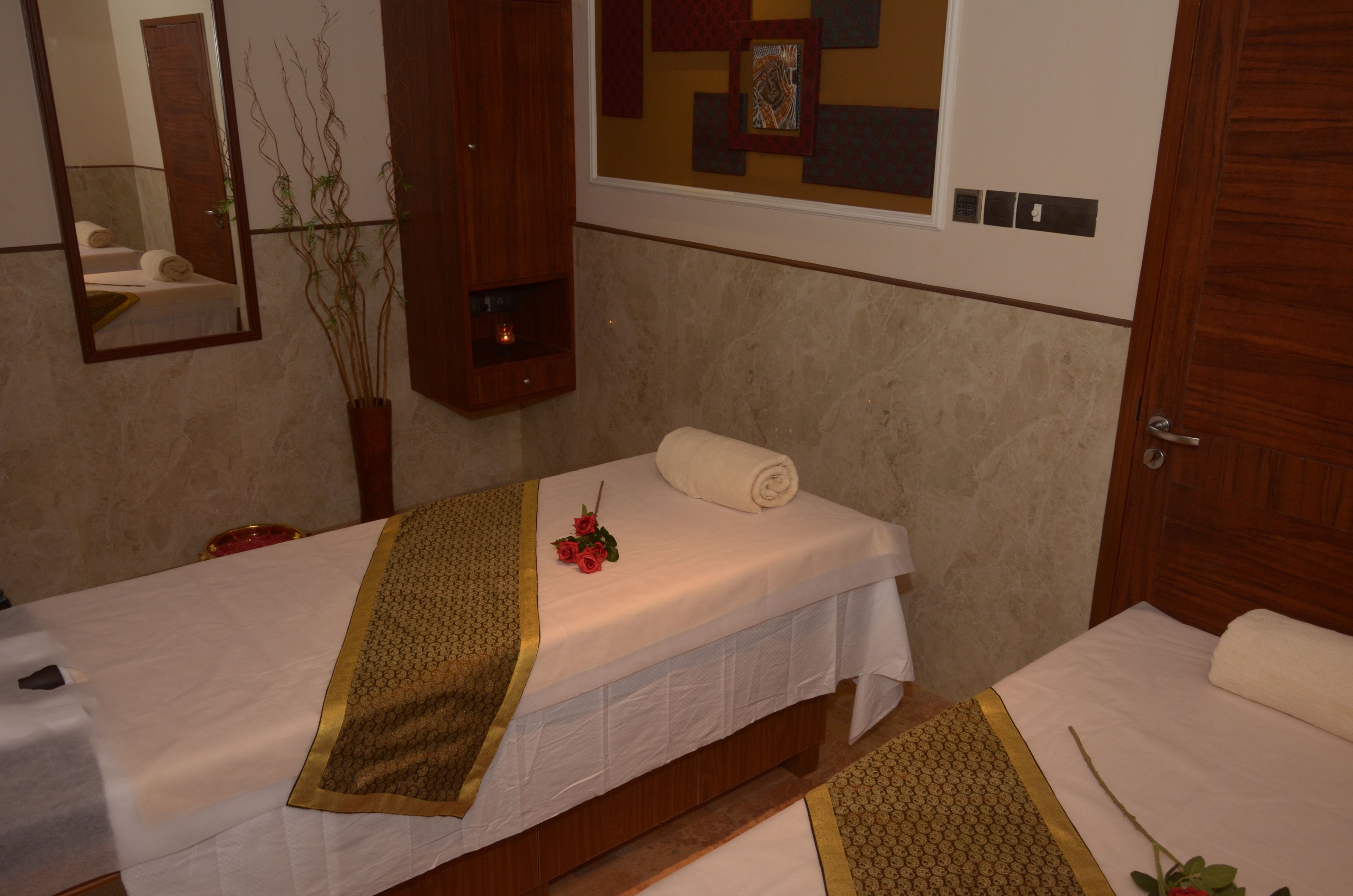 A spa room with two beds, a mirror, a wooden cabinet, and a wall with a geometric pattern.