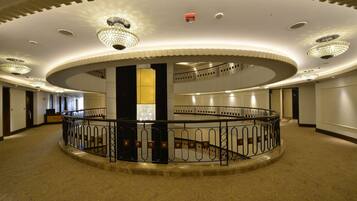 Un lobby espacioso y circular con una columna central, múltiples candelabros y una escalera de caracol.