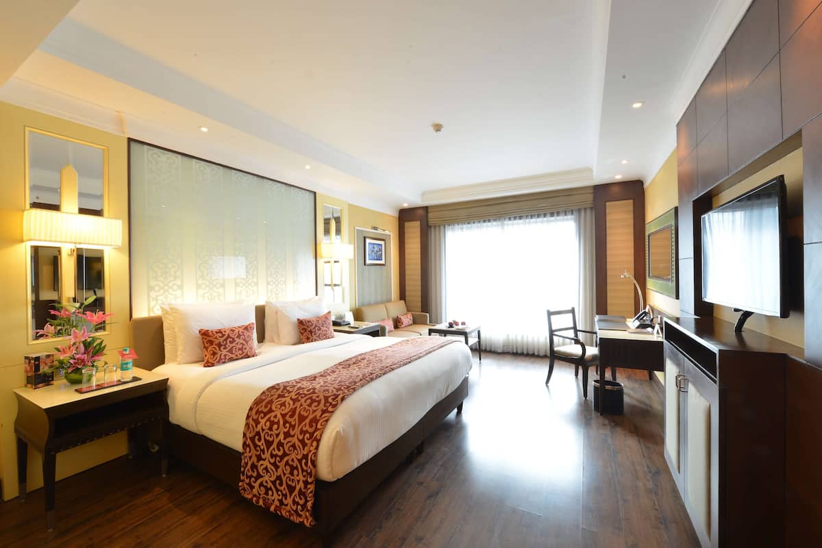Une chambre d’hôtel avec un grand lit, un bureau, une chaise, une télévision et une fenêtre avec des rideaux.