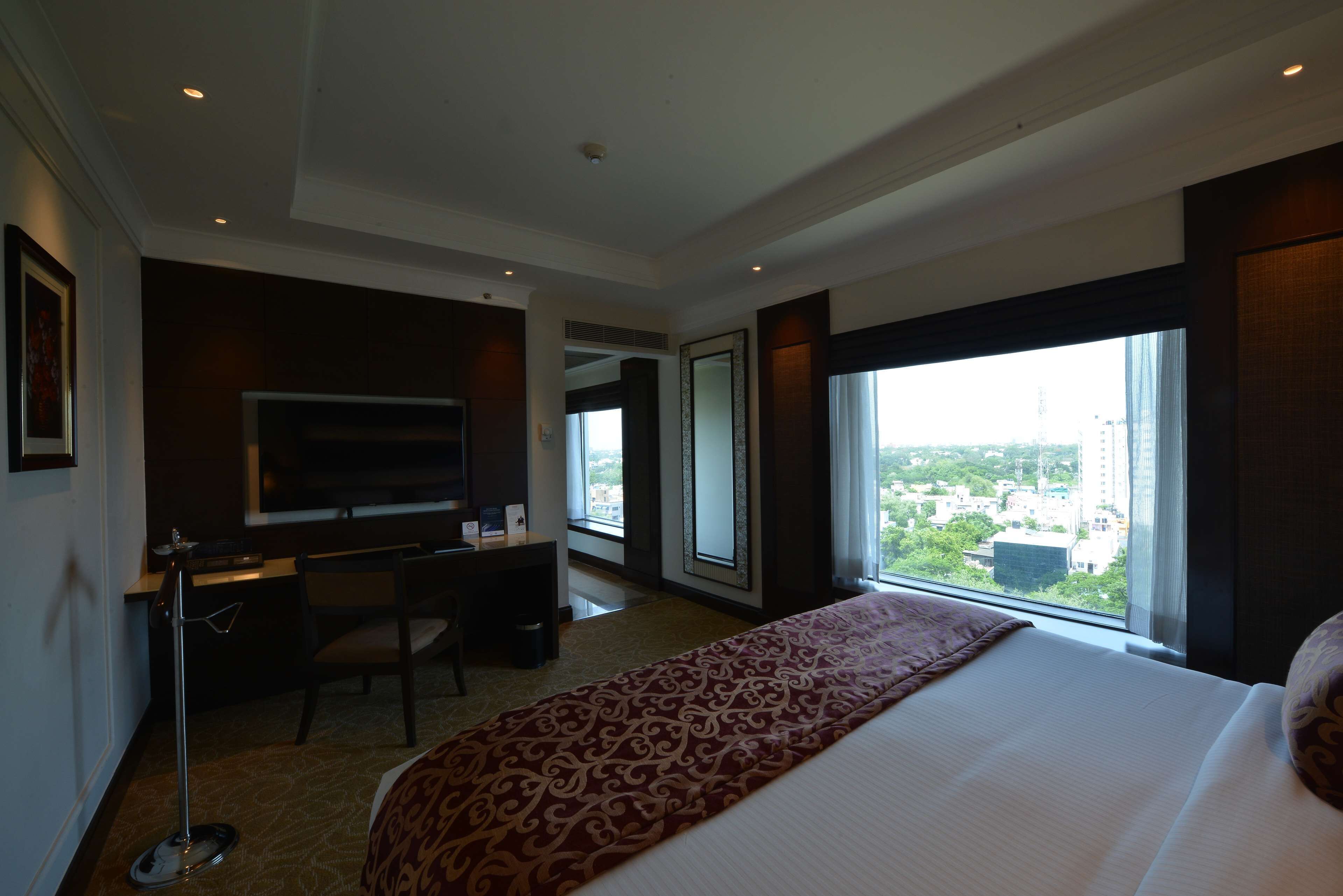 Une chambre d’hôtel avec un grand lit, un bureau, une chaise, une télévision et une fenêtre donnant sur la ville.