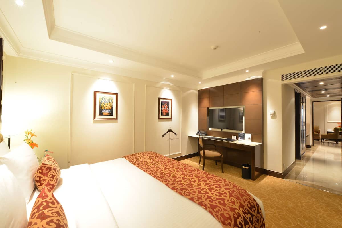 Une chambre d’hôtel avec un grand lit, un bureau avec un ordinateur, une télévision et des tableaux encadrés au mur.