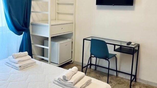 Habitación de hotel con cama, escritorio con silla, armario y televisor de pantalla plana en la pared.