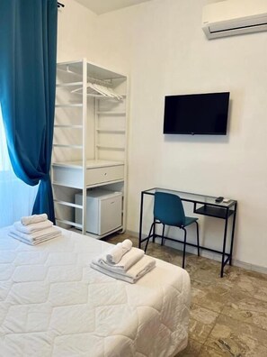 Une chambre d’hôtel comprenant un lit, un bureau avec une chaise, une armoire et un téléviseur à écran plat fixé au mur.