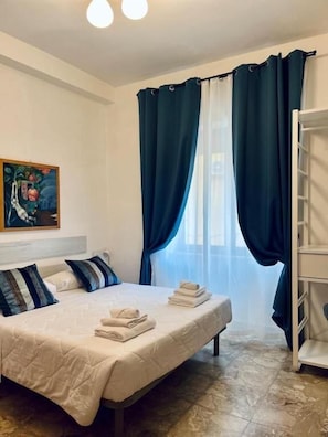 A neatly made bed with pillows, a painting on the wall, and a window with curtains. - Residence Mastrangelo (Naples)