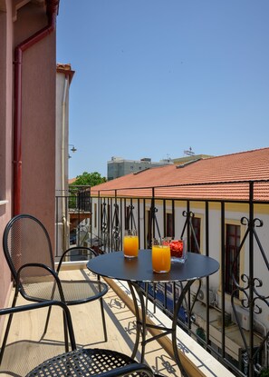 En balkon med et rundt bord og to stole, to glas appelsinjuice og en skål med snacks.