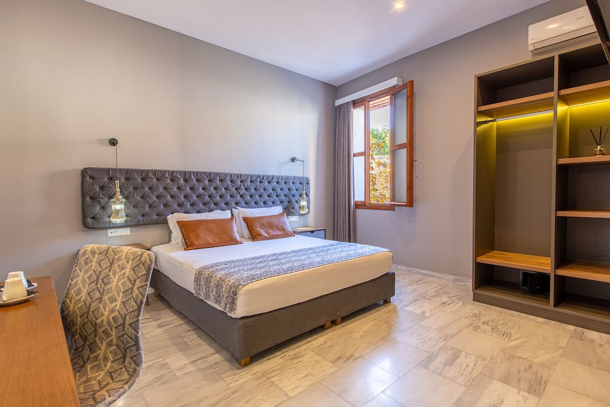 A modern bedroom with a tufted headboard, a large bed, a bedside table, a chair, a wardrobe, and a window with curtains.