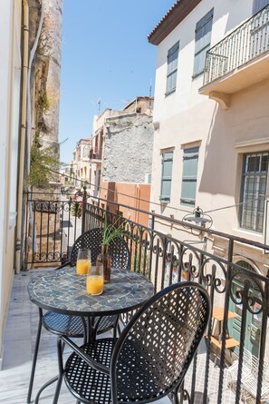 En balkon med et rundt bord, stole, en potteplante og et glas appelsinjuice.