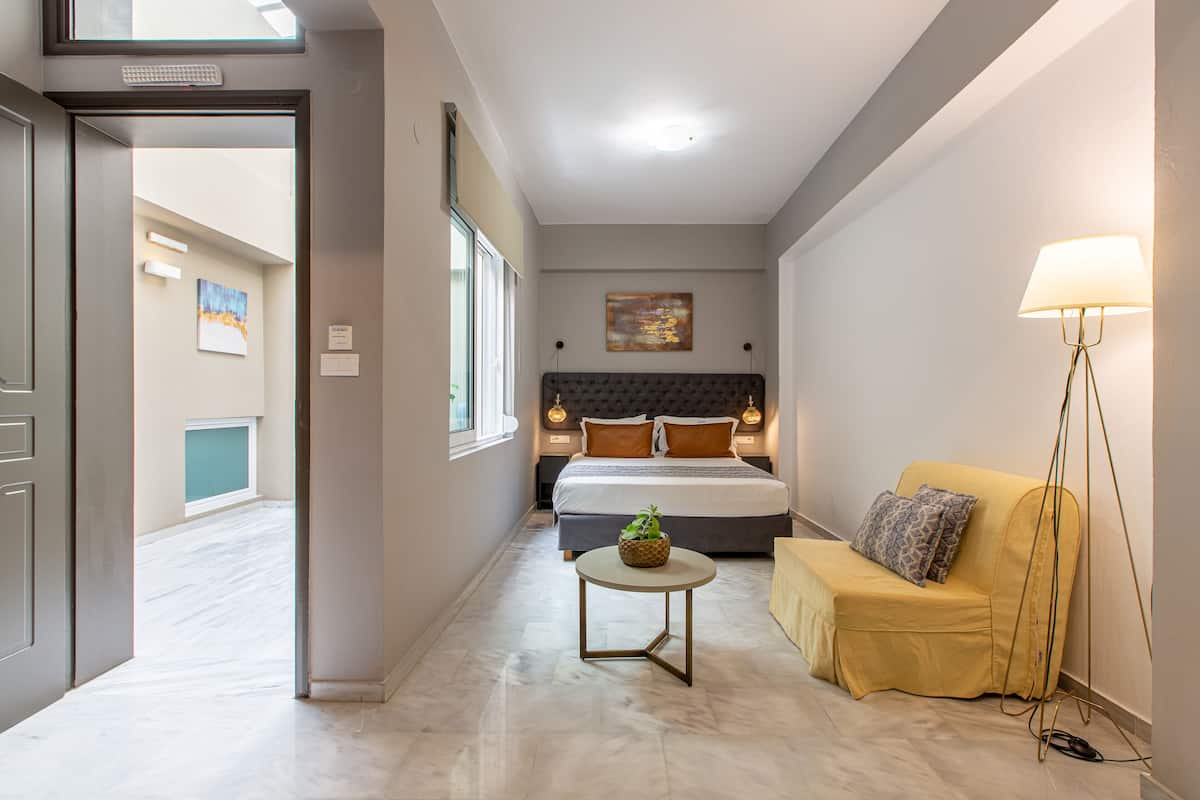 A hotel room with a bed, a bedside table, a lamp, and a sofa.