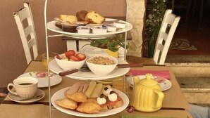 Une table dressée pour un repas, avec un présentoir à trois niveaux, des assiettes remplies de nourriture, une théière jaune et une paire de lunettes de soleil posées sur la table.
