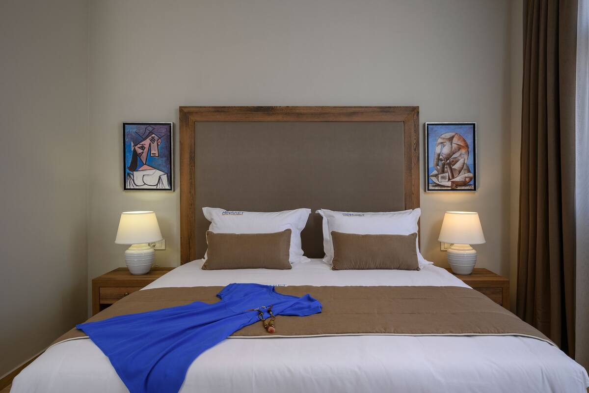 A neatly made bed with a blue blanket and pillows, wooden headboard, and two bedside lamps.