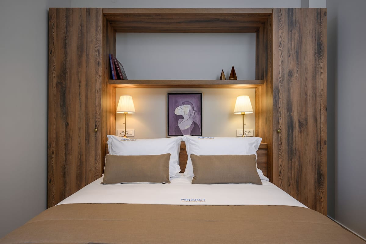 A neatly made bed with a white and brown color scheme, a framed artwork above it, and two bedside lamps.