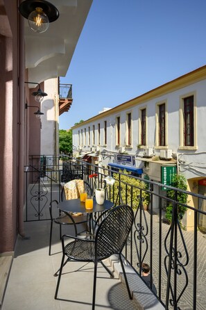A balcony with a table and chairs, a potted plant, and a view of a building with windows and balconies. - Minaret Suites & Apartments (Chania)