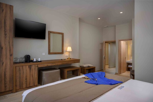 A hotel room with a bed, a desk with a flat-screen TV, a mirror, a lamp, and a wooden wardrobe.
