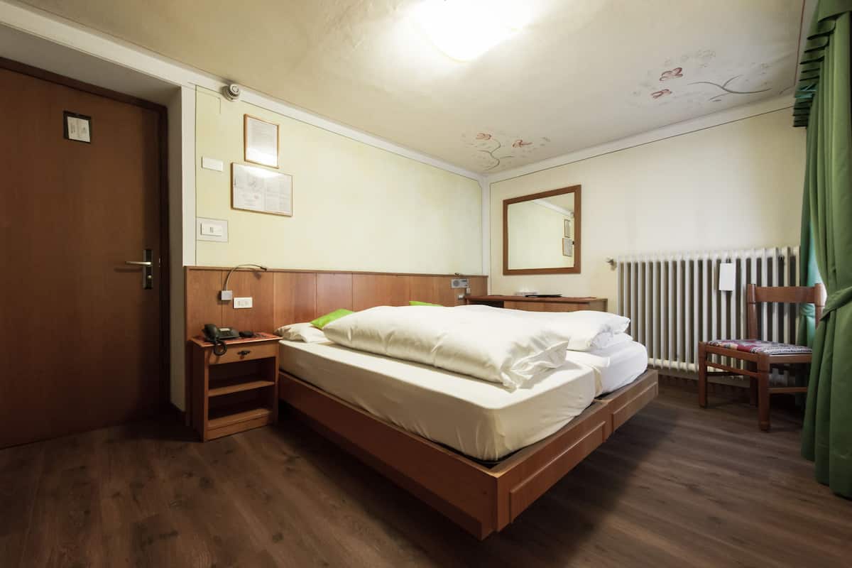 A bedroom with a wooden bed, a nightstand, a chair, a radiator, and a door.
