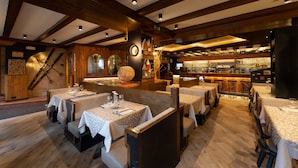 A restaurant with wooden beams, tables with white tablecloths, and a bar area. - Hotel Stella (Moena)