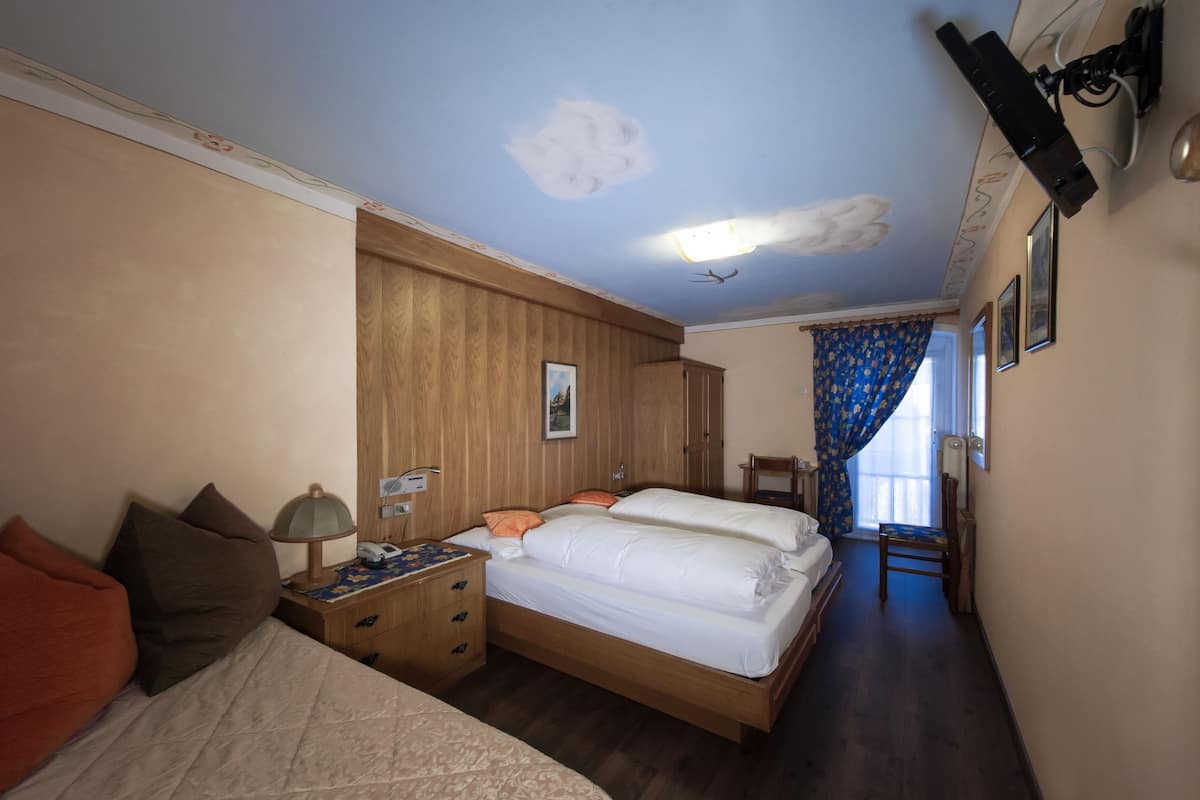 A bedroom with a wooden bed, a nightstand with a lamp, and a window with blue curtains.