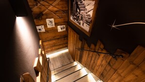 A wooden staircase with a metal handrail, wooden walls, and framed pictures. - Hotel Stella (Moena)