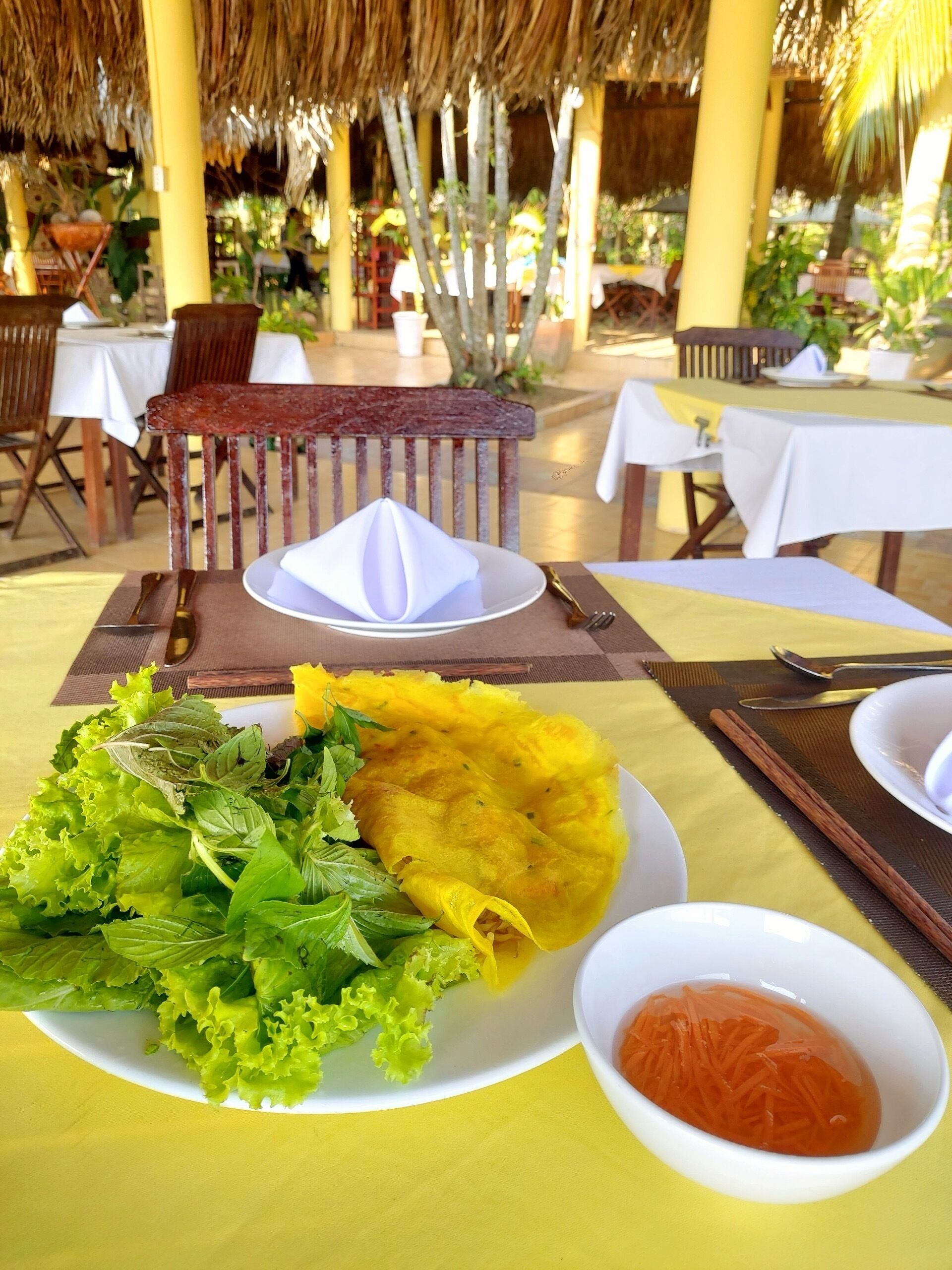 A dining table with a plate of food, a bowl of sauce, and a yellow wrap.