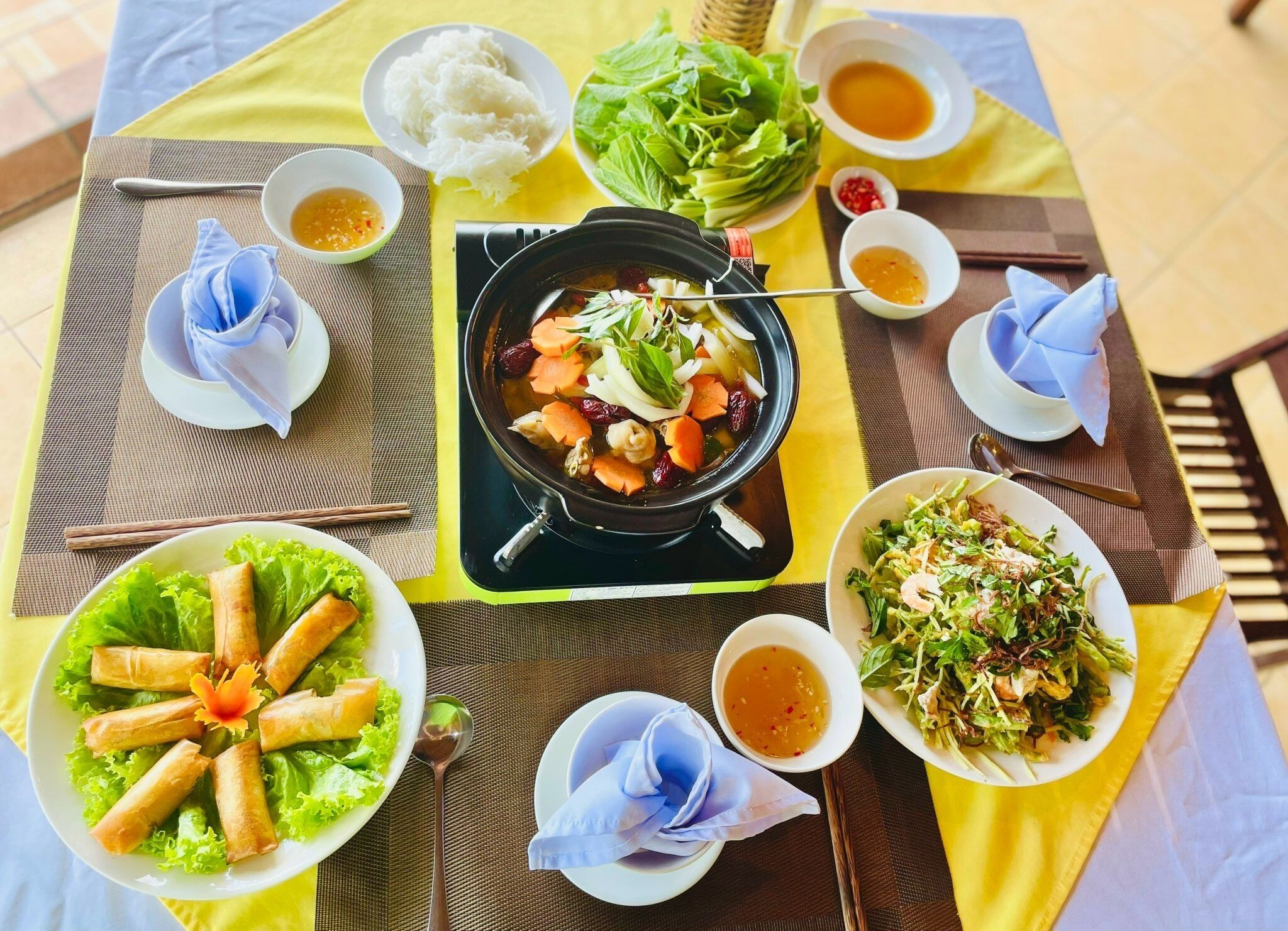 A table set with various dishes including a hot pot, spring rolls, and a salad, suggesting a meal setup.