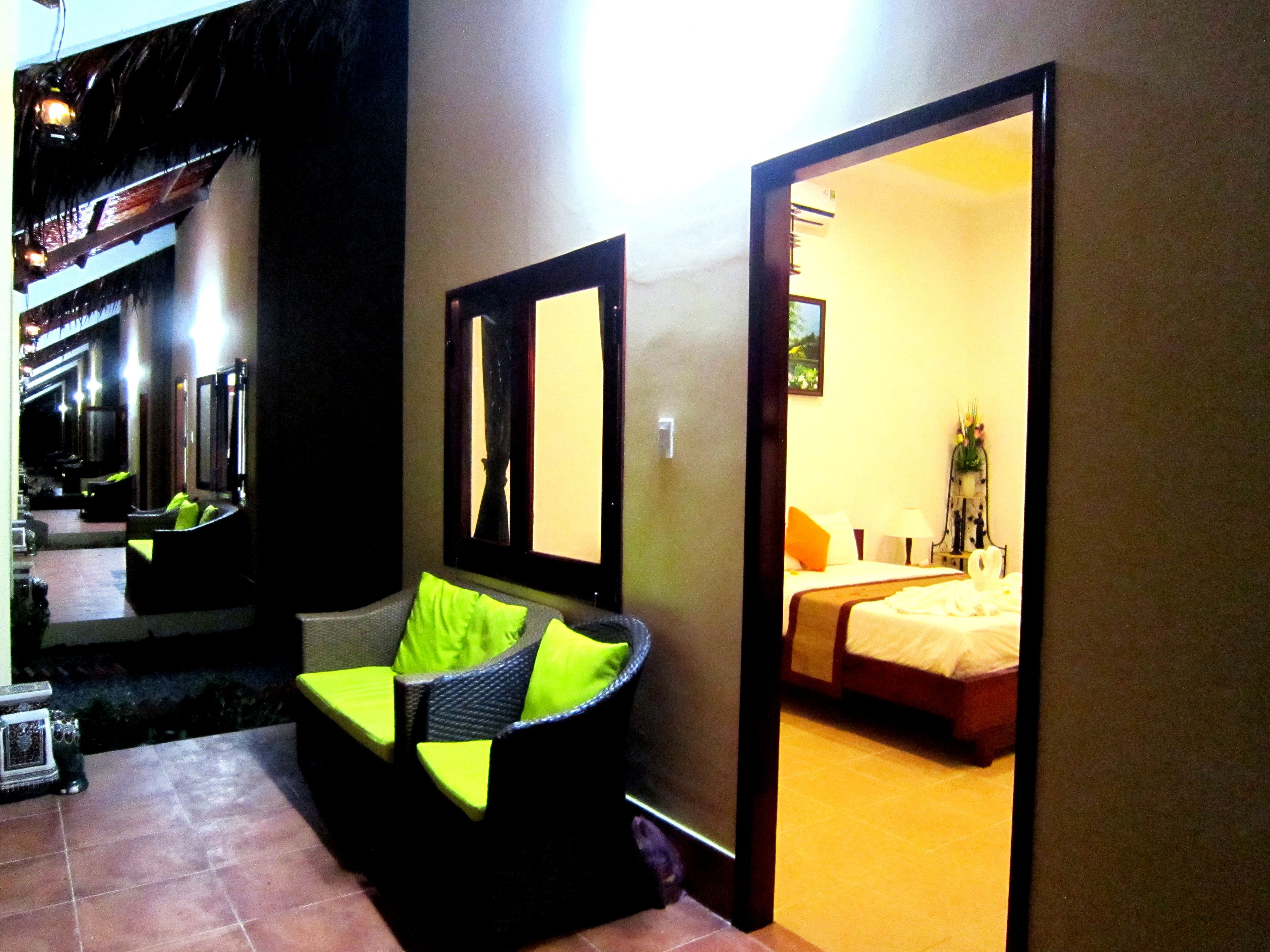 A hotel room with a bed, a seating area with cushions, a mirror, and a view of the outside.