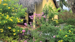 A thatched-roof house surrounded by lush greenery and flowering plants.