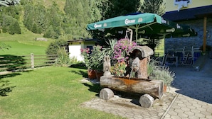 Un área de estar rústica al aire libre con una estructura de madera, un parasol verde y una pared de piedra al fondo.