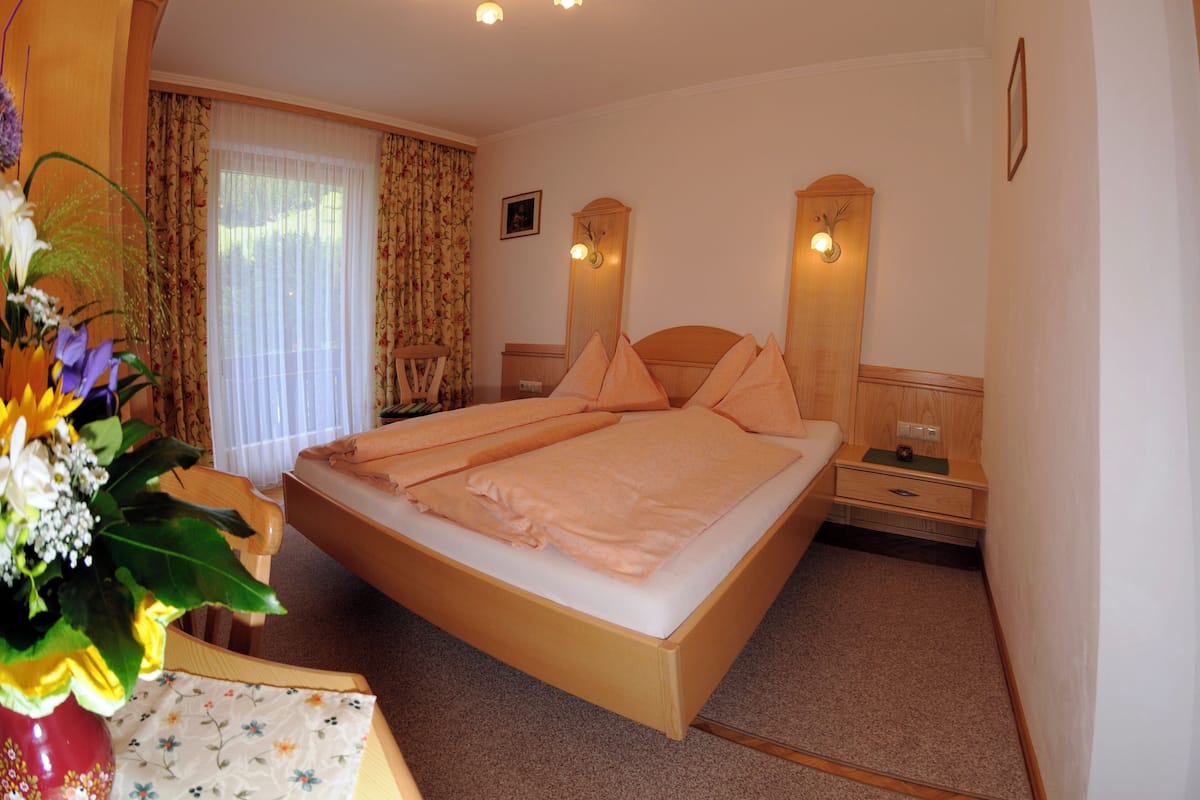 Ein ordentlich eingerichtetes Schlafzimmer mit einem Bett, Nachttischen, einem Spiegel und einem Fenster mit Vorhängen.