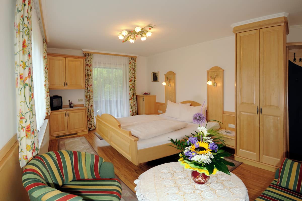 Ein Schlafzimmer mit einem Bett, einem Holzschrank, einem kleinen Tisch mit Blumenvase und einem Fernseher auf einem Schrank.