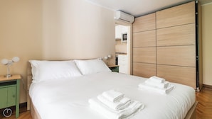 A neatly made bed with white linens and towels, a bedside table with a lamp, and a wooden wardrobe with a mirror. - Italianway   - Lazzaro Palazzi (Milan)