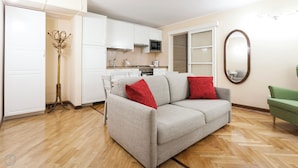 A compact living space with a kitchenette, a sofa with red cushions, a green armchair, and a large mirror on the wall. - Italianway   - Lazzaro Palazzi (Milan)
