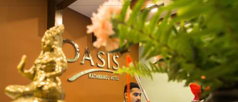 Mostrador de recepción en el Hotel Kathmandu con una estatua dorada, una recepcionista y un cartel.