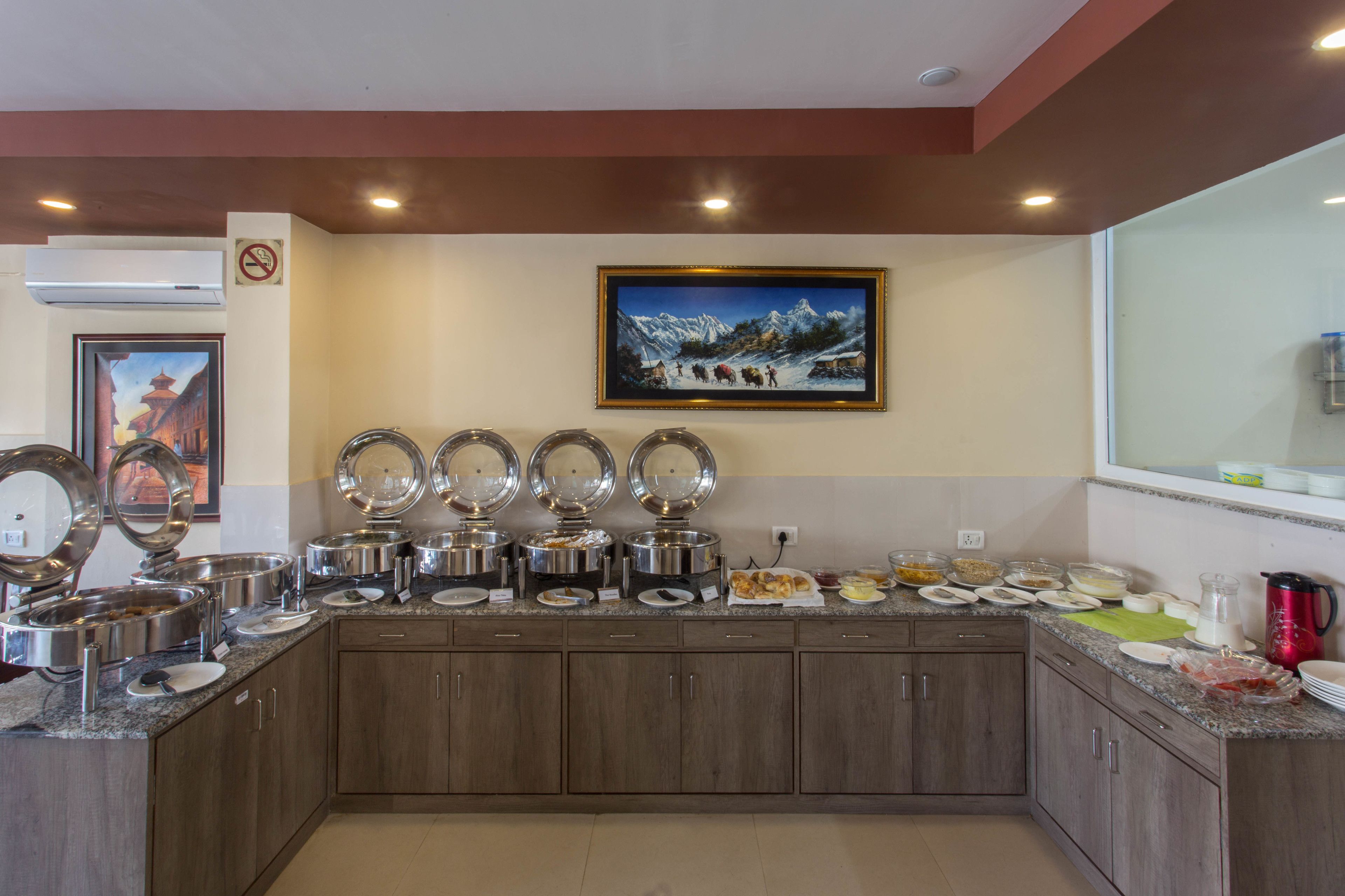 Un buffet avec plusieurs points de service, un tableau représentant un paysage de montagne enneigé et un panneau «interdiction de fumer» accroché au mur.