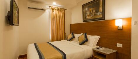 A hotel room with a bed, a nightstand, a painting, an air conditioner, and a window with curtains.