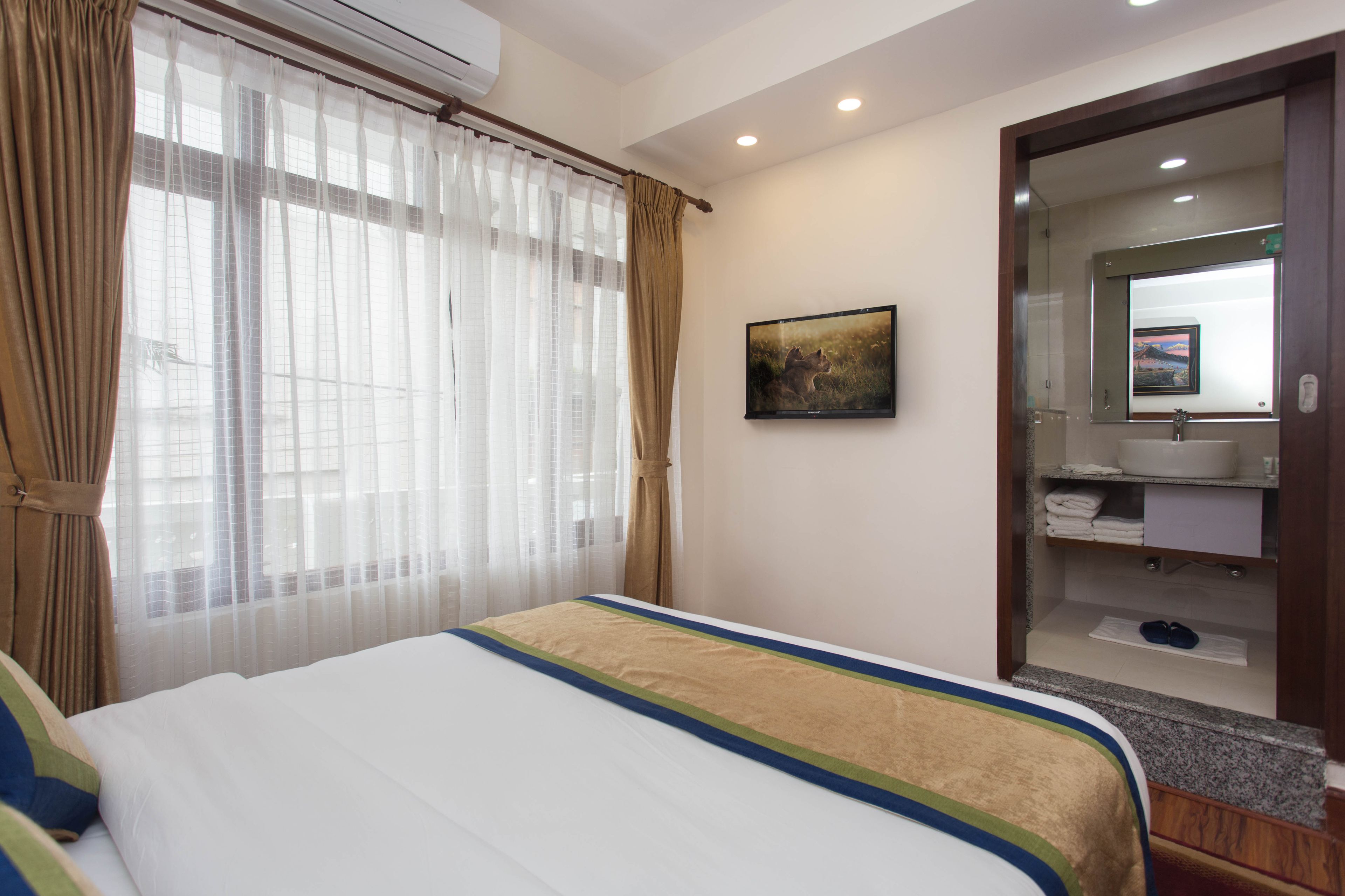 Hotelkamer met een bed, een groot raam met dunne gordijnen, een schilderij aan de muur, en een badkamer met spiegel en wastafel.