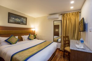 Habitación de hotel con cama, escritorio, silla, espejo y equipo de aire acondicionado.