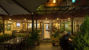 Un área de comedor al aire libre con mesas, sillas, plantas en macetas y una zona de estar cubierta.