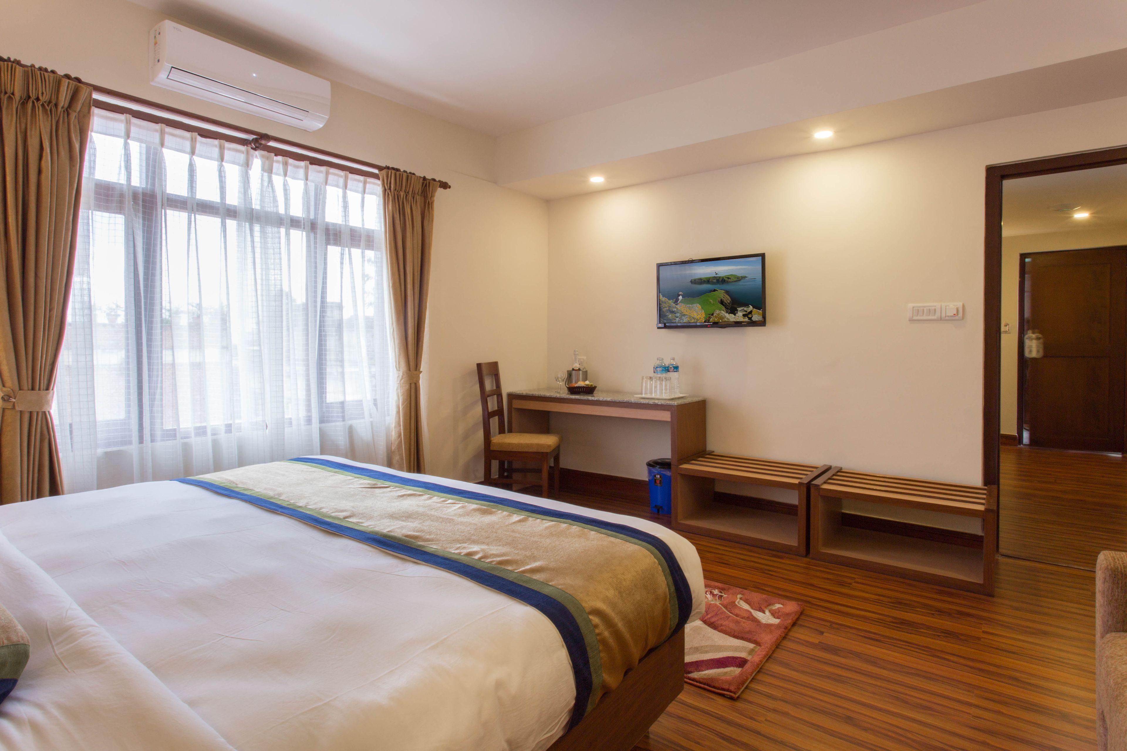 Een hotelkamer met een groot bed, een bureau, een stoel, een klein bankje en een schilderij aan de muur.