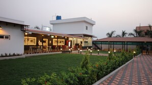 A modern building with a covered outdoor seating area, a well-maintained lawn, and a brick pathway. - Hotel Majestique pune (Pune)