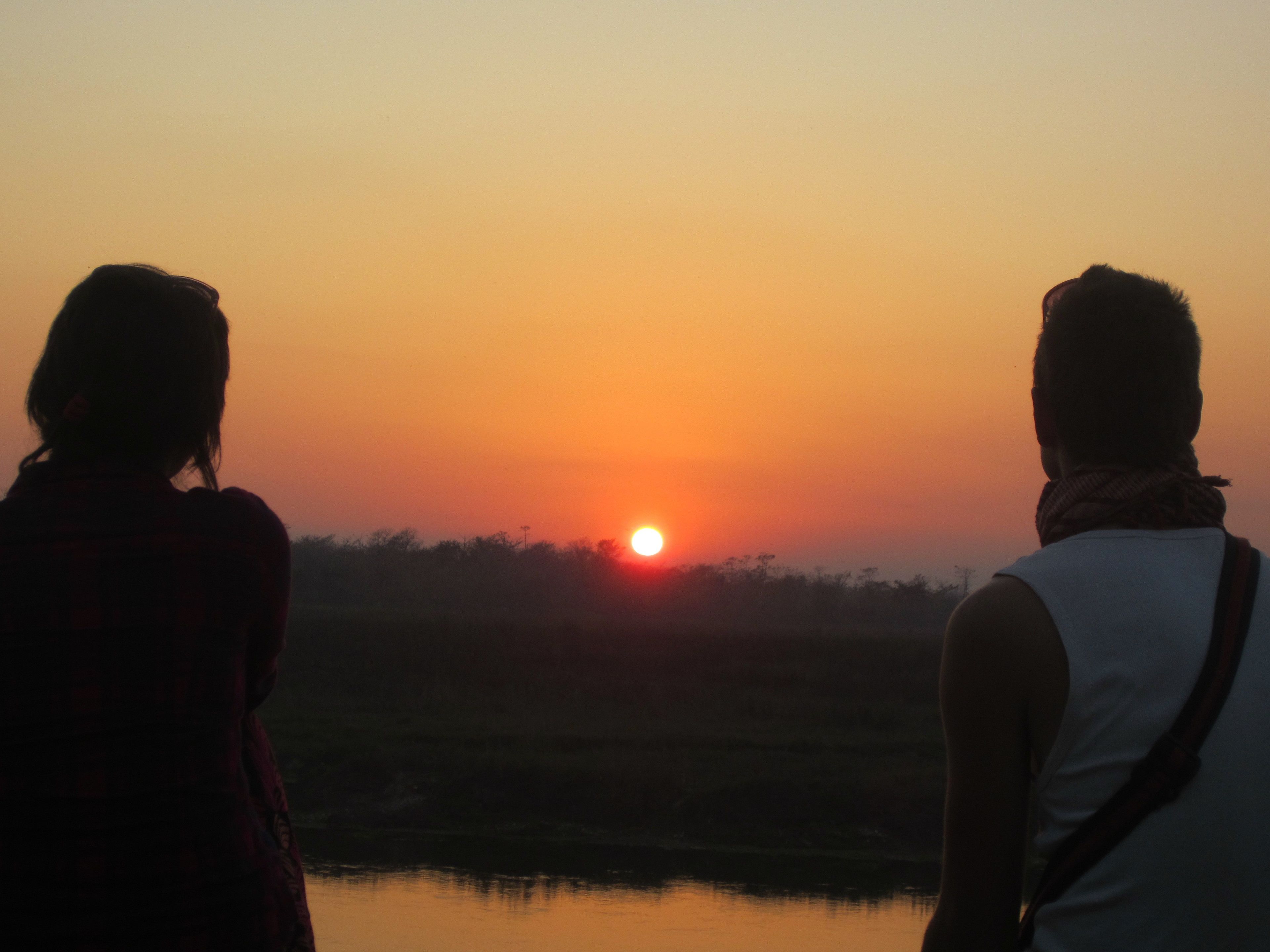 Two people standing by a body of water during sunset.