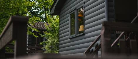 A wooden cabin with a window, a staircase, and a view of trees.