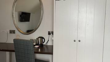 Una habitación con escritorio, silla, armario, espejo y televisor.